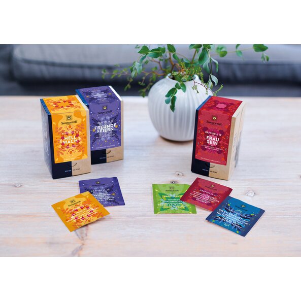 A picture of three Happiness Is packs. The teas are on a round table, together with a plant.